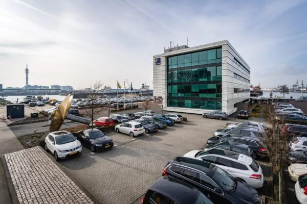 Kantoorpand met glazen gevel en parkeerplaats bij de Waalhaven in Rotterdam, met uitzicht op de haven en schepen.